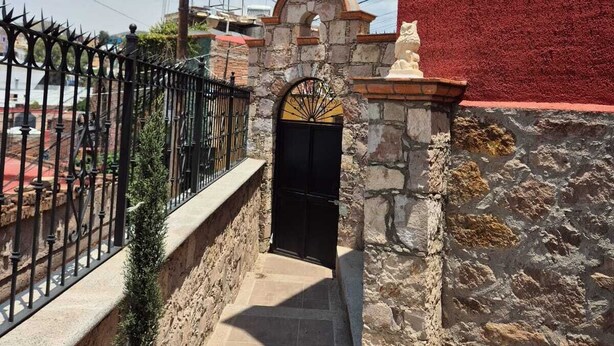 A stone entrance with a black gate, a small archway, and a cross above it.