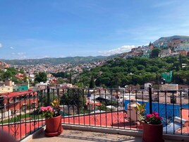 A balcony with a view of a densely populated cityscape, including buildings and greenery.