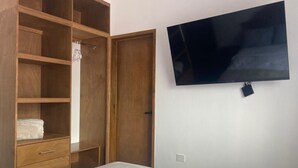 A bedroom with a bed, wooden wardrobe, and a flat-screen TV mounted on the wall.