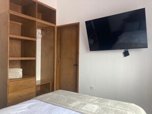 A bedroom with a bed, wooden wardrobe, and a flat-screen TV mounted on the wall.