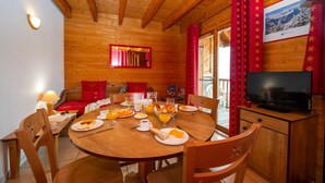 A wooden cabin interior with a dining table set for breakfast, a television, and a view of a snowy landscape. - Goelia - Le Village Gaulois (Saint-François-Longchamp)