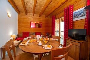 A wooden cabin interior with a dining table set for breakfast, a television, and a view of a snowy landscape. - Goelia - Le Village Gaulois (Saint-François-Longchamp)