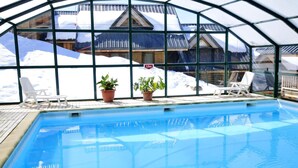 An indoor swimming pool with clear glass walls, potted plants, and lounge chairs.