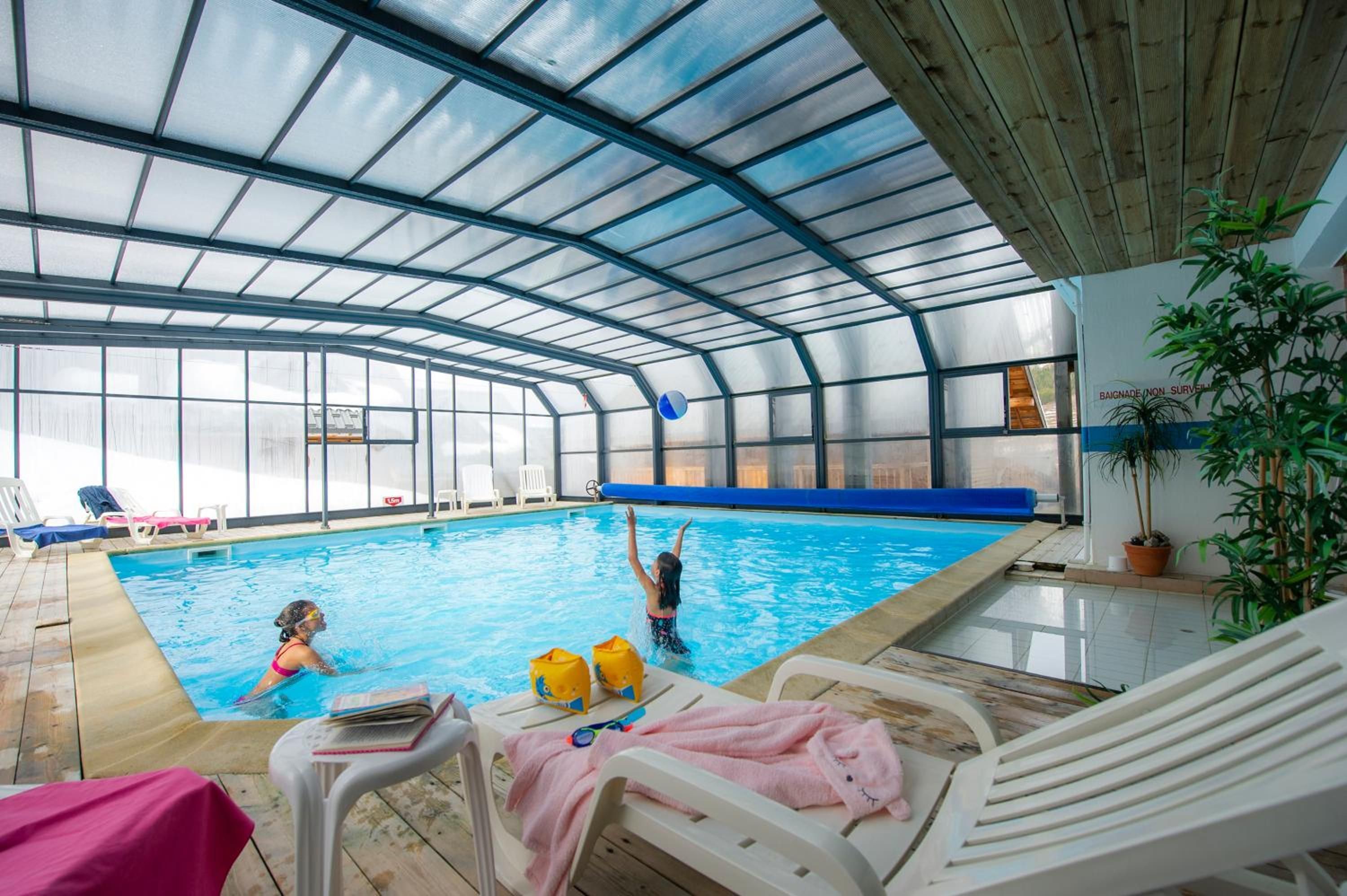 An indoor swimming pool with a glass ceiling, lounge chairs, and a poolside table.