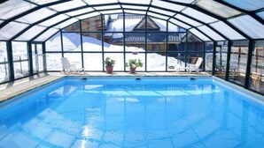 An indoor swimming pool with clear glass walls, a wooden deck, and lounge chairs.