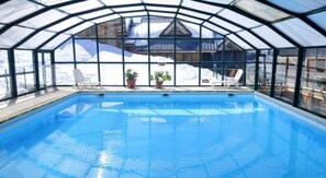 An indoor swimming pool with clear glass walls, a wooden deck, and lounge chairs. - Goelia - Le Village Gaulois (Saint-François-Longchamp)