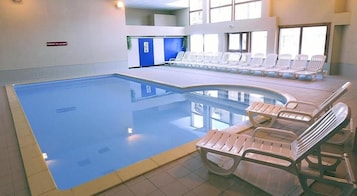 Piscina interna com espreguiçadeiras e piso azulejado azul.