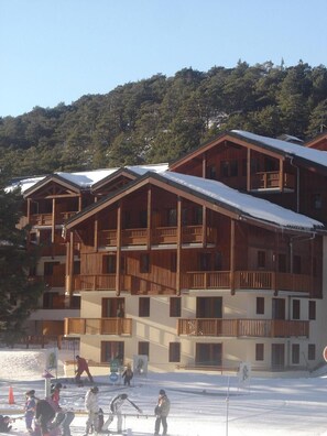 A multi-story wooden building with balconies, likely a hotel or resort, with a snowy landscape in the background. - Goelia - Les Balcons D'anaes (Villarodin-Bourget)