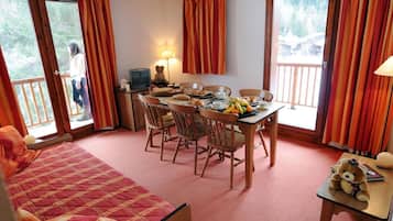 Een gezellige kamer met een bed, een eettafel met stoelen, een televisie en een raam met gordijnen.