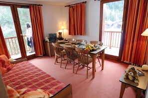 A cozy room with a bed, a dining table with chairs, a television, and a window with curtains. - Goelia - Les Balcons D'anaes (Villarodin-Bourget)