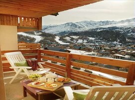 Un balcon en bois offrant une vue sur des montagnes enneigées et un village situé en contrebas.