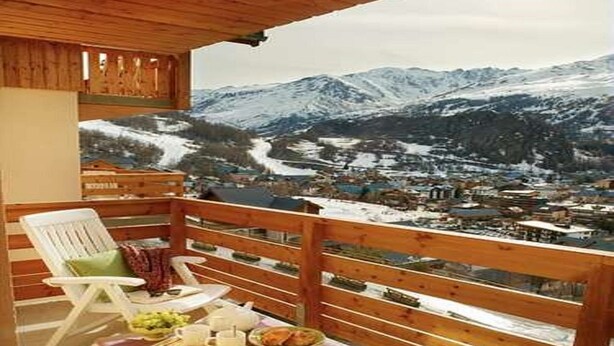Een houten balkon met uitzicht op besneeuwde bergen en een dorp beneden.