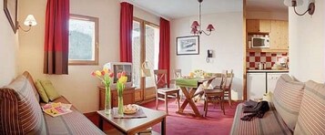 Un salon confortable avec un canapé, une table à manger et des chaises. On aperçoit une cuisine au fond.