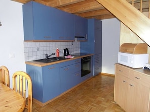 Eine kleine Küche mit blauen Schränken, einem Holztisch und einer Mikrowelle.