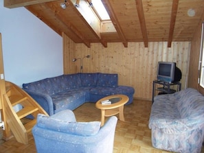 Ein Zimmer mit Holzbalkendecke, einem blauen Sofa, einem Holztisch und einem Fernseher auf einem Schrank.
