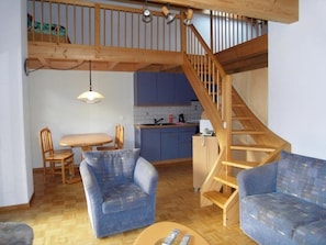 Ein Wohnbereich im Loft-Stil mit einer Holztreppe, einem Esstisch, zwei blauen Sesseln und einer Küche im Hintergrund.