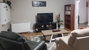 Una sala de estar con televisión, estantería, radiador y sofá.