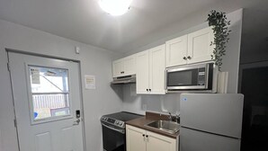 Cocina compacta con armarios blancos, microondas, estufa y refrigerador.