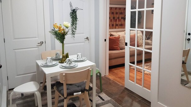 Un comedor con una mesa dispuesta para dos, un florero con flores y vista a una sala de estar con sofá y cojines.