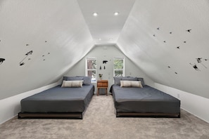 Ein kleines, modernes Schlafzimmer mit zwei Betten, einem Nachttisch und einem Fenster mit Blick auf Bäume.