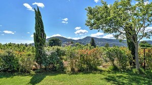 Un jardin luxuriant, avec une grande variété d’arbres et d’arbustes, une pelouse bien entretenue et une vue lointaine sur des montagnes sous un ciel dégagé.