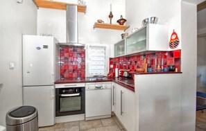 Una cocina compacta con refrigerador, horno y microondas. Hay estantes de madera sobre la encimera y un salpicadero de baldosas rojas.