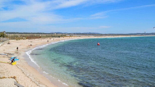 Une plage à l’eau claire, une bouée rouge et une côte lointaine.