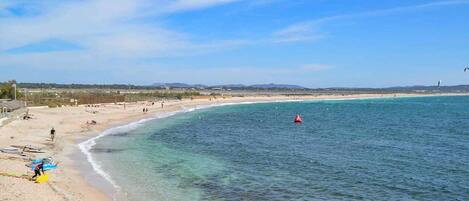 A beach with clear water, a red buoy, and a distant shoreline.