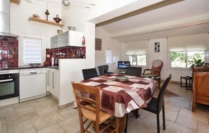 A kitchen with white cabinets, a dining table with chairs, a television, and a window with blinds.