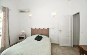 Un dormitorio con cama, mesita de noche, unidad de aire acondicionado, puerta y ventana con cortinas.