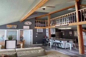 A spacious living area with a high ceiling, a balcony, and a kitchen area.