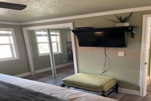 Une chambre à coucher comprenant un lit, un téléviseur fixé au mur, une porte-fenêtre coulissante et un petit tabouret.