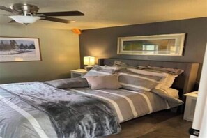 Un dormitorio con cama, mesitas de noche, ventilador de techo y un cuadro enmarcado en la pared.