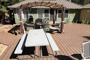 Un área de comedor al aire libre techada con una mesa de picnic, sillas y una parrilla.