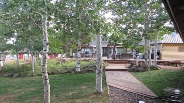 Ein Garten mit einer Holzterrasse, Bäumen und einem Haus im Hintergrund.