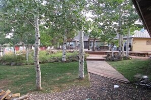 Ein Garten mit einer Holzterrasse, Bäumen und einem Haus im Hintergrund.