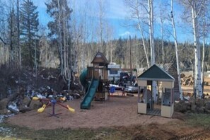 Ein Spielplatz mit Rutsche und Schaukeln, einer kleinen Schutzhütte und einem Bereich mit Erde.
