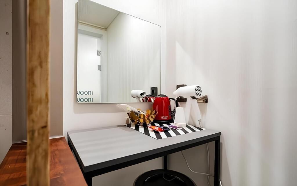 A hotel room with a mirror, a small table with a red kettle, and two hair dryers.