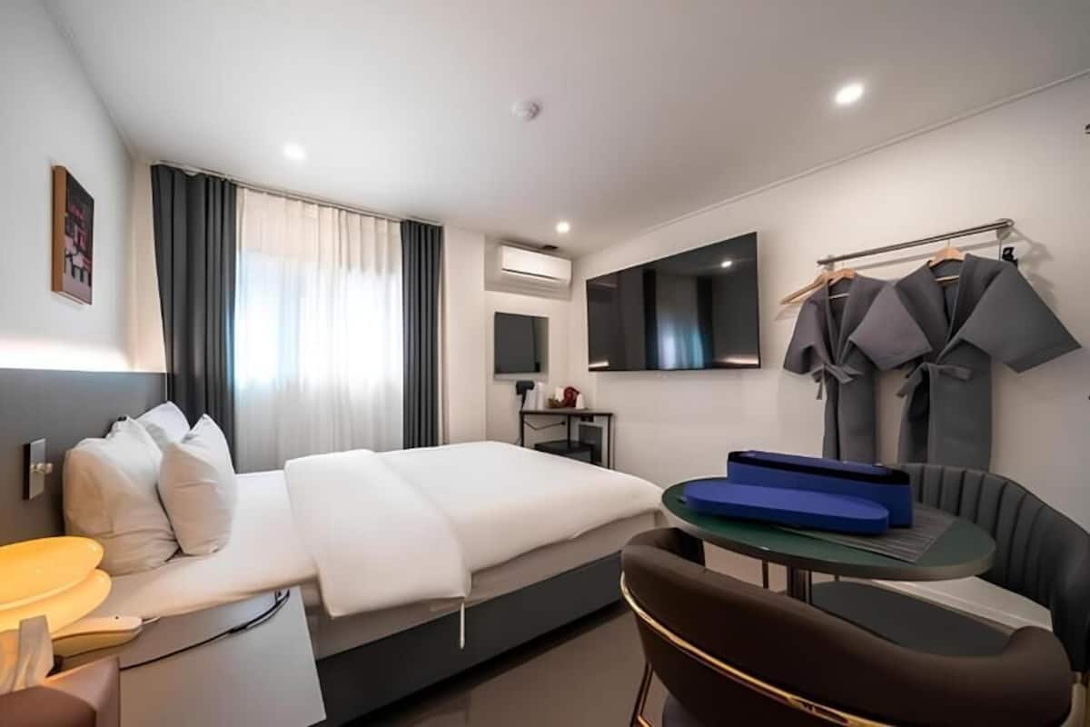 Una habitación de hotel moderna con cama, mesita de noche, silla, escritorio y televisión.