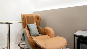 Una silla moderna con cojín, una mesita pequeña y un armario en una habitación con pared lisa.