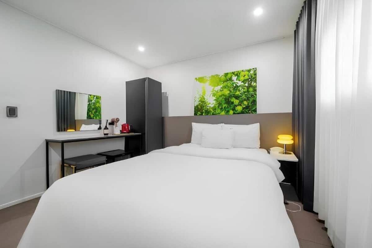 Habitación de hotel moderna con una cama grande, un escritorio con silla, un espejo y una ventana con vistas a zonas verdes.