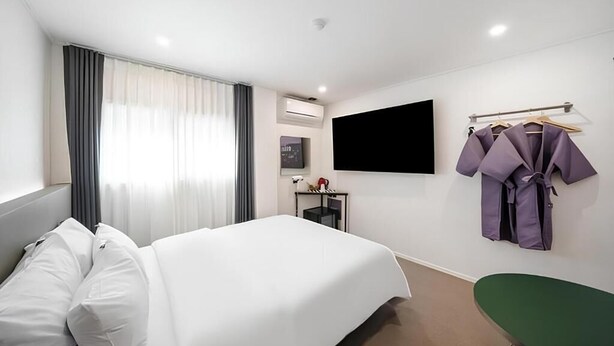 Habitación de hotel con cama, escritorio, silla, televisor y perchero para bata.