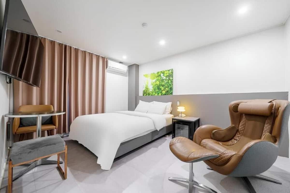 Una habitación de hotel moderna con cama, escritorio, silla, mesita de noche y televisor montado en la pared.