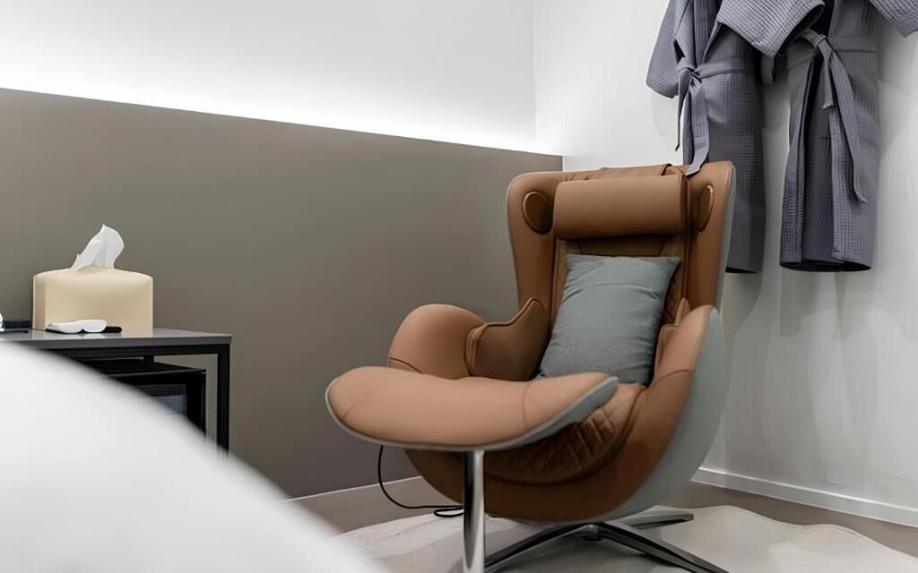 A modern chair with a cushion, a candle, and a robe on the wall.