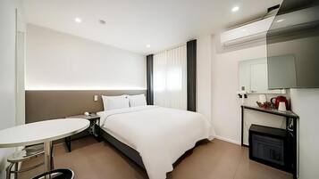 Una habitación de hotel moderna con cama, mesita de noche y un pequeño escritorio con silla.