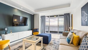 Ein modernes Wohnzimmer mit einem Flachbildfernseher, einer Couch, einem Couchtisch und Meerblick durch große Fenster.