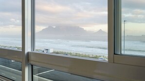 Blick durch ein Fenster auf die Küste, mit einer Straße, einem Strand und fernen Bergen.