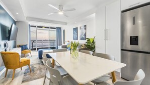 Eine moderne Küche mit einem Edelstahl-Kühlschrank, eine Essecke mit weißem Tisch und Stühlen und ein großes Fenster mit Blick.
