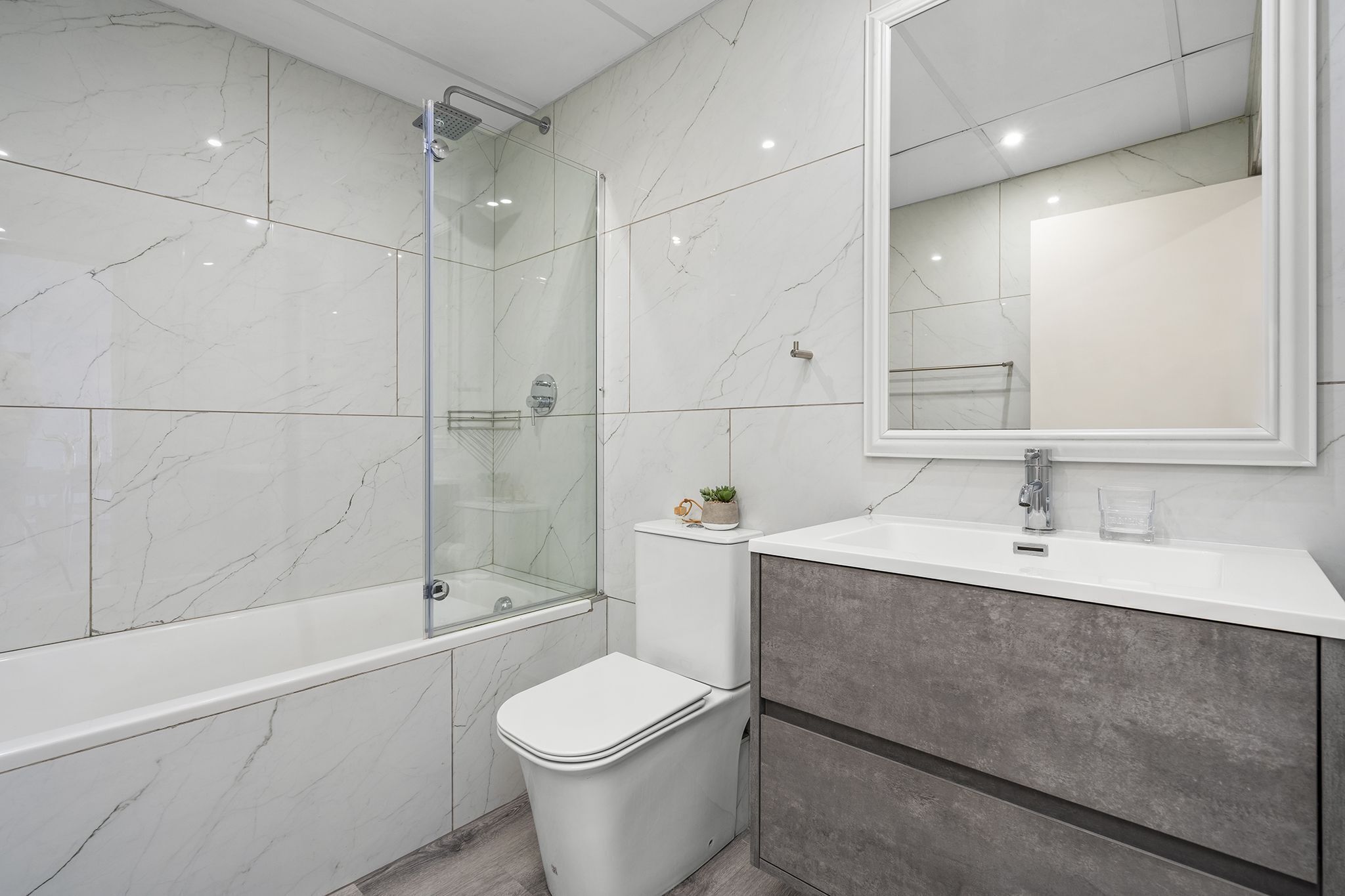 Une salle de bain moderne avec une douche à parois de verre, des toilettes blanches, un meuble-lavabo avec un miroir et des carreaux de marbre.