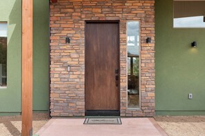 A wooden door with a stone facade, a doormat, and a small window to the right. - New Luxury Home – Special Introductory Pricing for a Limited Time. (Sedona)